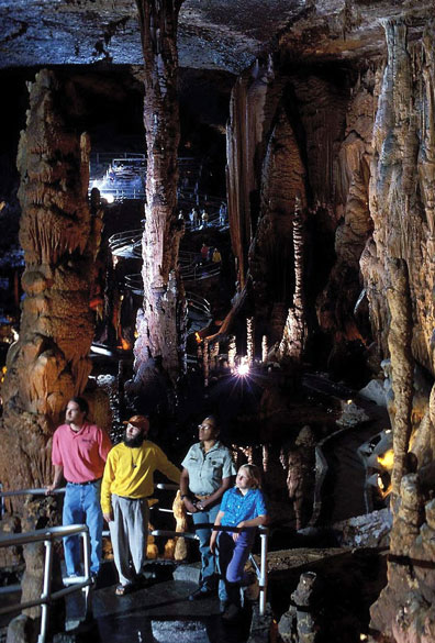 Interior of a large cave with rock formations and tourists walking along a paved path with railings