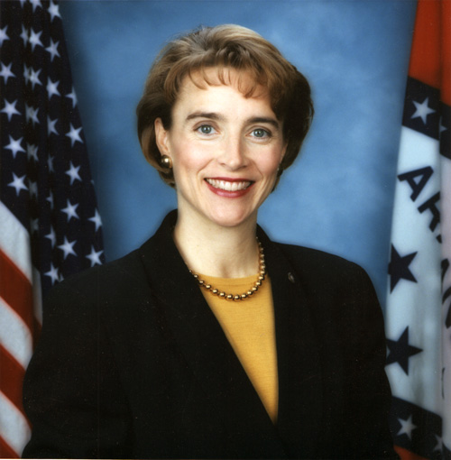 Portrait of white woman in suit with U.S. and Arkansas flag backdrop