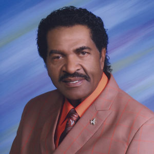 African-American man with mustache in smiling in suit and tie