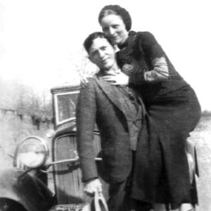 Young white man holding a young white woman posing with car