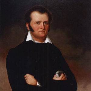 White man with brown hair and sideburns in black with white collar