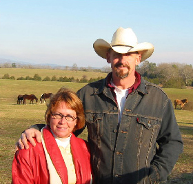 white woman and white man in cowboy hat in pasture with horses in background