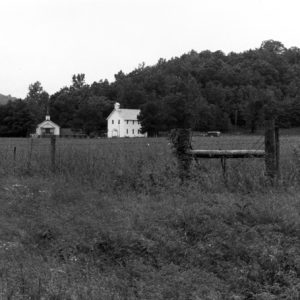 Farm field with fence buildings in background along mountain ridge
