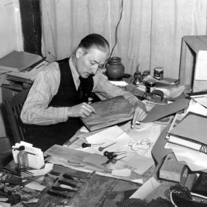 White man in long-sleeved shirt and vest working at his desk