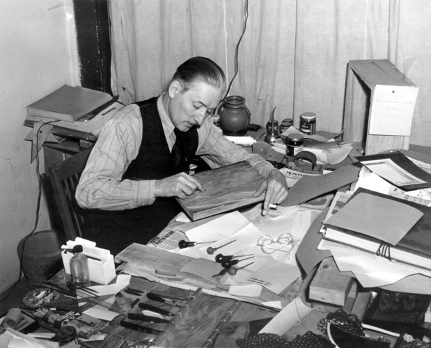 White man in long-sleeved shirt and vest working at his desk