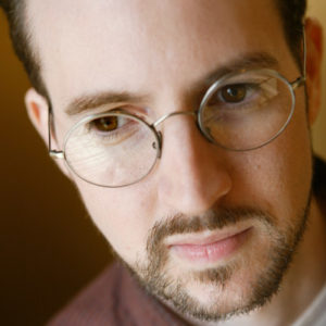 Portrait white man round glasses short hair and beard collared shirt focused expression downward angle