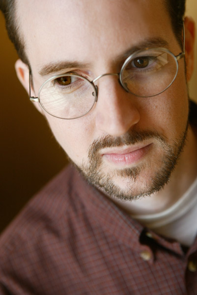 Portrait white man round glasses short hair and beard collared shirt focused expression downward angle