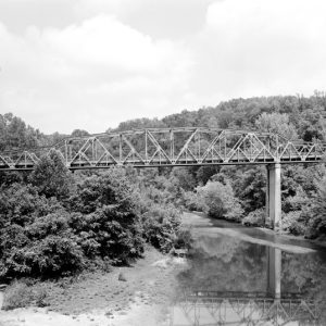 Steel bridge spanning river with sand bar trees in foreground and mountain ridge behind