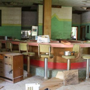 Tall chairs at counter inside abandoned restaurant with debris on the floor