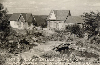 Pair of cabin buildings with rock walls and foot bridge over creek in the foreground