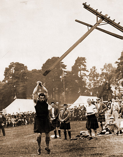 White man in kilt tossing a telephone pole as white spectators watch with tents in the background