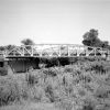 Steel and concrete river bridge with overgrown embankment and trees