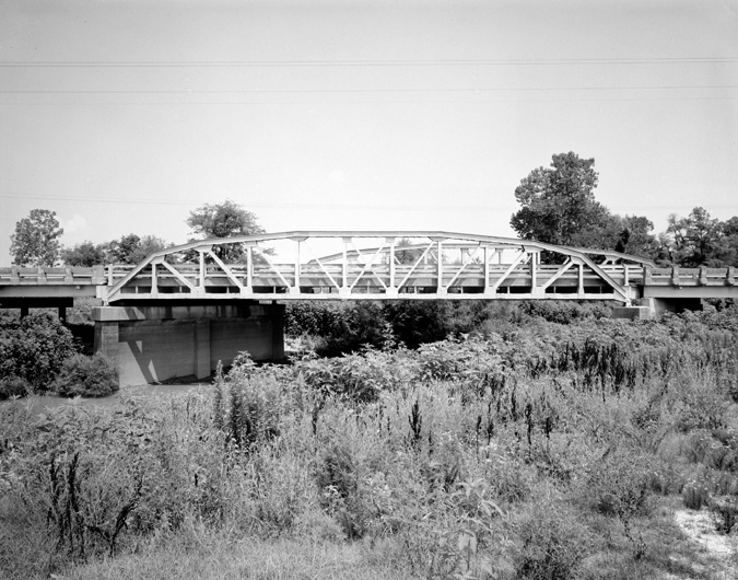 Steel and concrete river bridge with overgrown embankment and trees