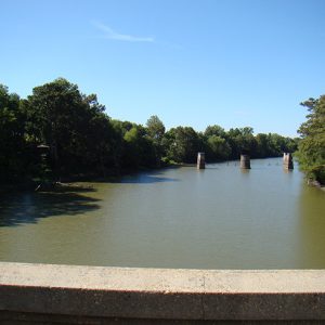 View of river as seen from concrete bridge with three former bridge supports in the distance