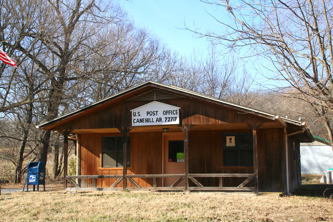 rustic wooden building surrounded by trees with sign reading "U.S. Post Office Canehill, AR. 72717"