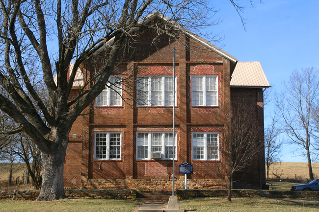 two-story brick building with flagpole and tree