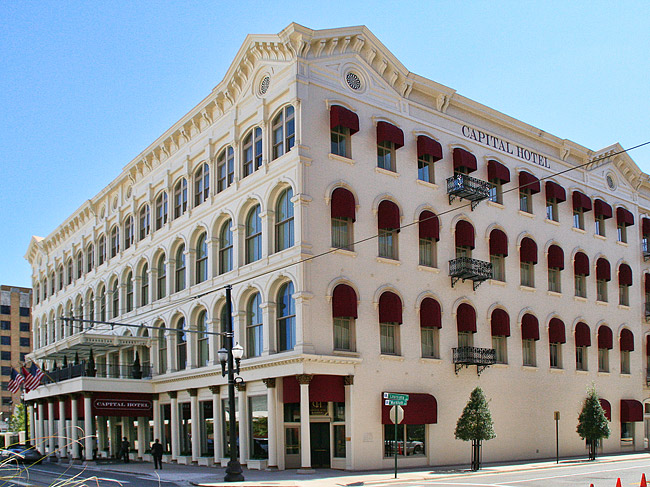 four-story white stone building with red awnings over each side window and words "Capital Hotel" at top