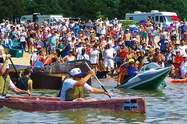 White men racing cardboard boats with crowd