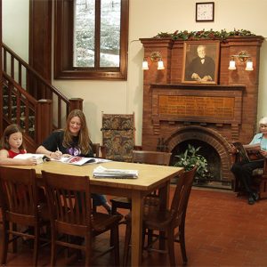 White woman and girl studying in library with painting of Andrew Carnegie on fireplace