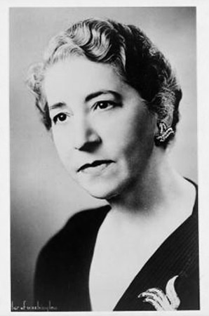 portrait photo of serious-faced white woman with curly hair and black dress with pin