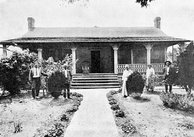 Three black men and two black women pose in landscaped yard outside home with wide porch