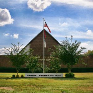 brick building with pointed roof and flagpole behind small sign reading "Central Baptist College"
