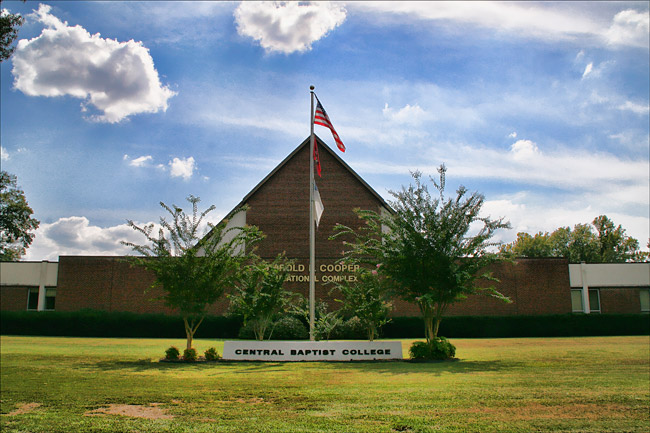 brick building with pointed roof and flagpole behind small sign reading "Central Baptist College"