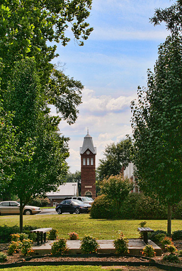 brick bell tower in distance behind parking lot and landscaping with benches and trees