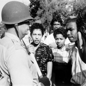 white man in helmet with gun faces group of African American teens
