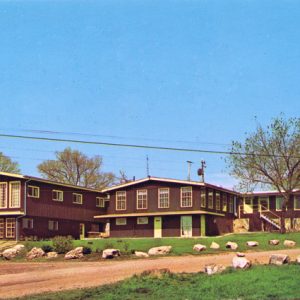 Wood frame lodge and boulder lined gravel road with cars trees