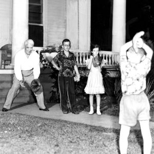 White man, two white boys, and white girl play catch with ball and gloves by front porch