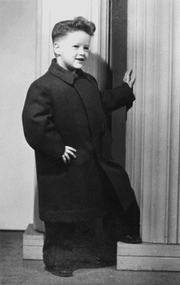 Portrait young boy posing smiling in matching shoes slacks long jacket foot hand on column