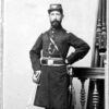 Bearded white man in military uniform with sword posing next to banister