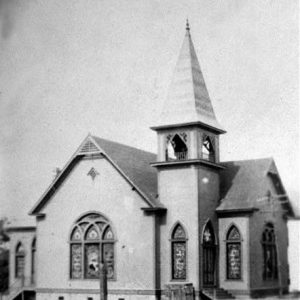 Single-story church building with arched stained glass windows and bell tower