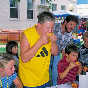 White children eating peaches with white man and building behind them