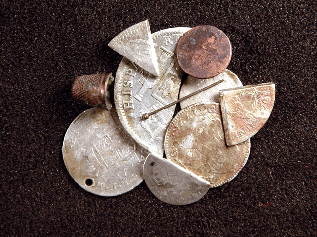 Stack of coins and coin pieces with thimble and metal pin