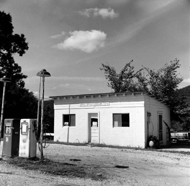 Two gas pumps with light poles outside small cinder block building with angled wood frame roof