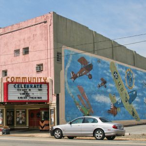 Multistory brick storefronts and "Community" movie theater with airplane mural painted on its side wall