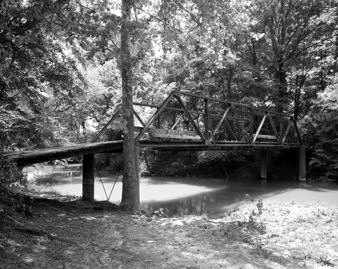 Narrow steel bridge with wooden slats over  wooded creek
