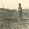 Man wearing hat and vest standing in dirt field