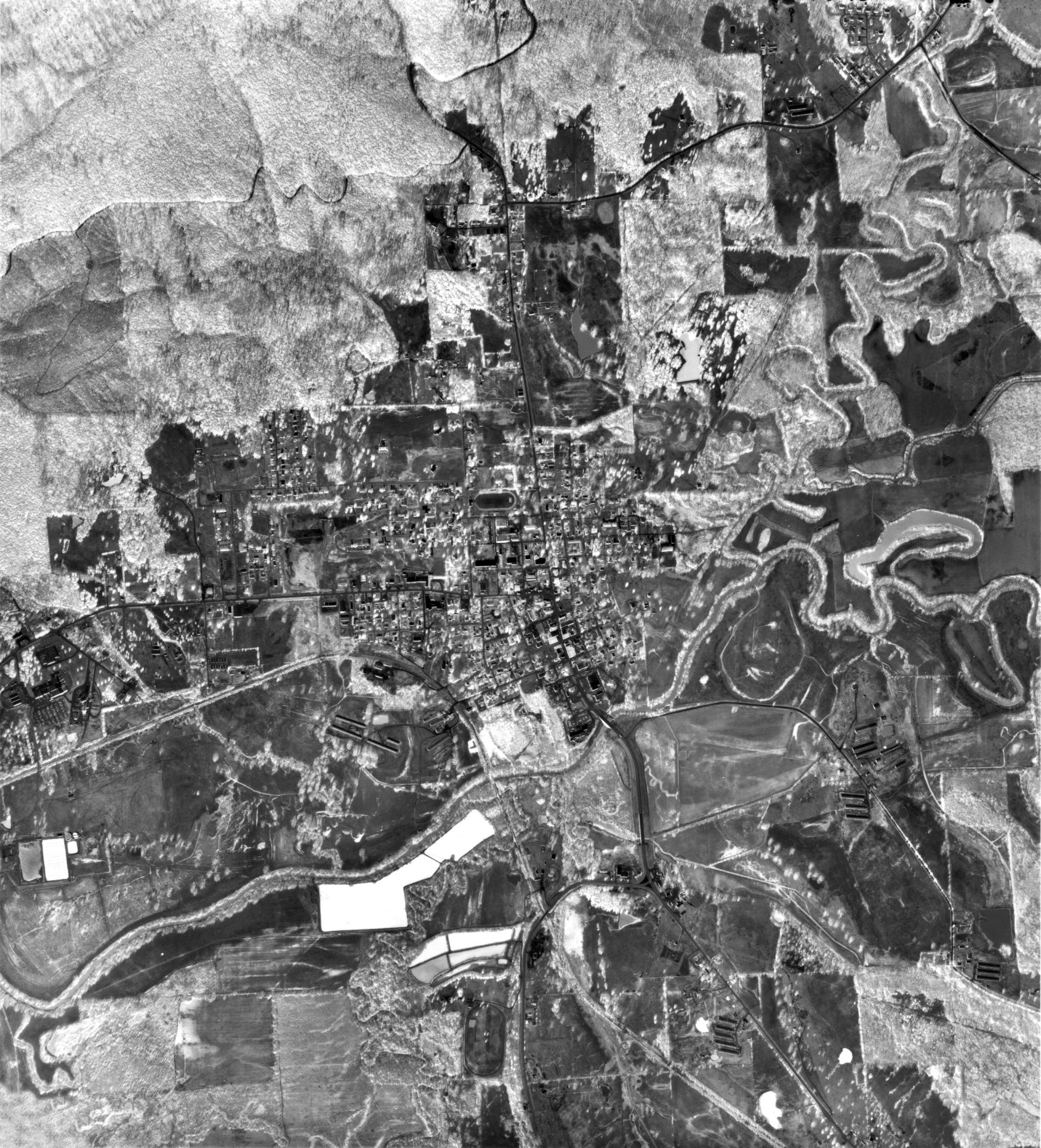 Aerial view of city with suburb above farmland below with railroad river and broad forest