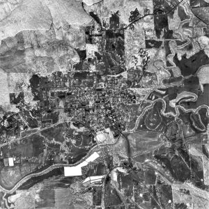 Aerial view of city with suburb above farmland below with railroad river and broad forest