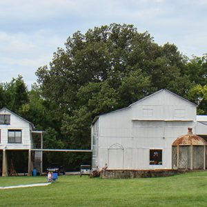 House on stilts next to barn shaped building on grass