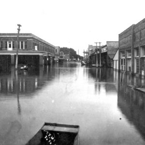 A flooded downtown city block photographed from a small boat pictured in the foreground.
