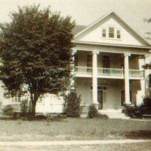 Three-story house with balcony and columns and trees on either side