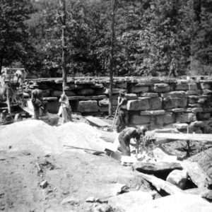 Stone wall construction with workers and machinery in forest