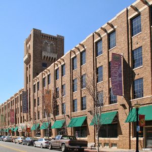 long four-story brick building with small tower and many large windows, cars parked in parallel in front of it