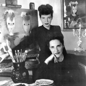 Two white women posing with paintings and paintbrushes