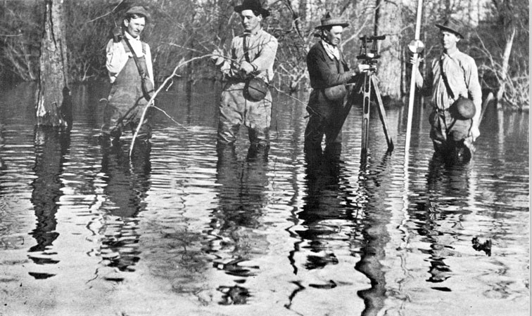 Four white men with surveying equipment standing in water