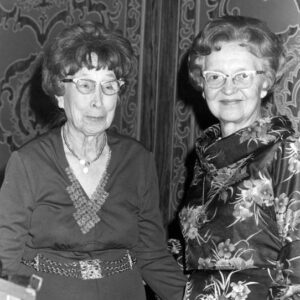 Old white woman in glasses smiling next to old white woman with glasses smiling in floral dress